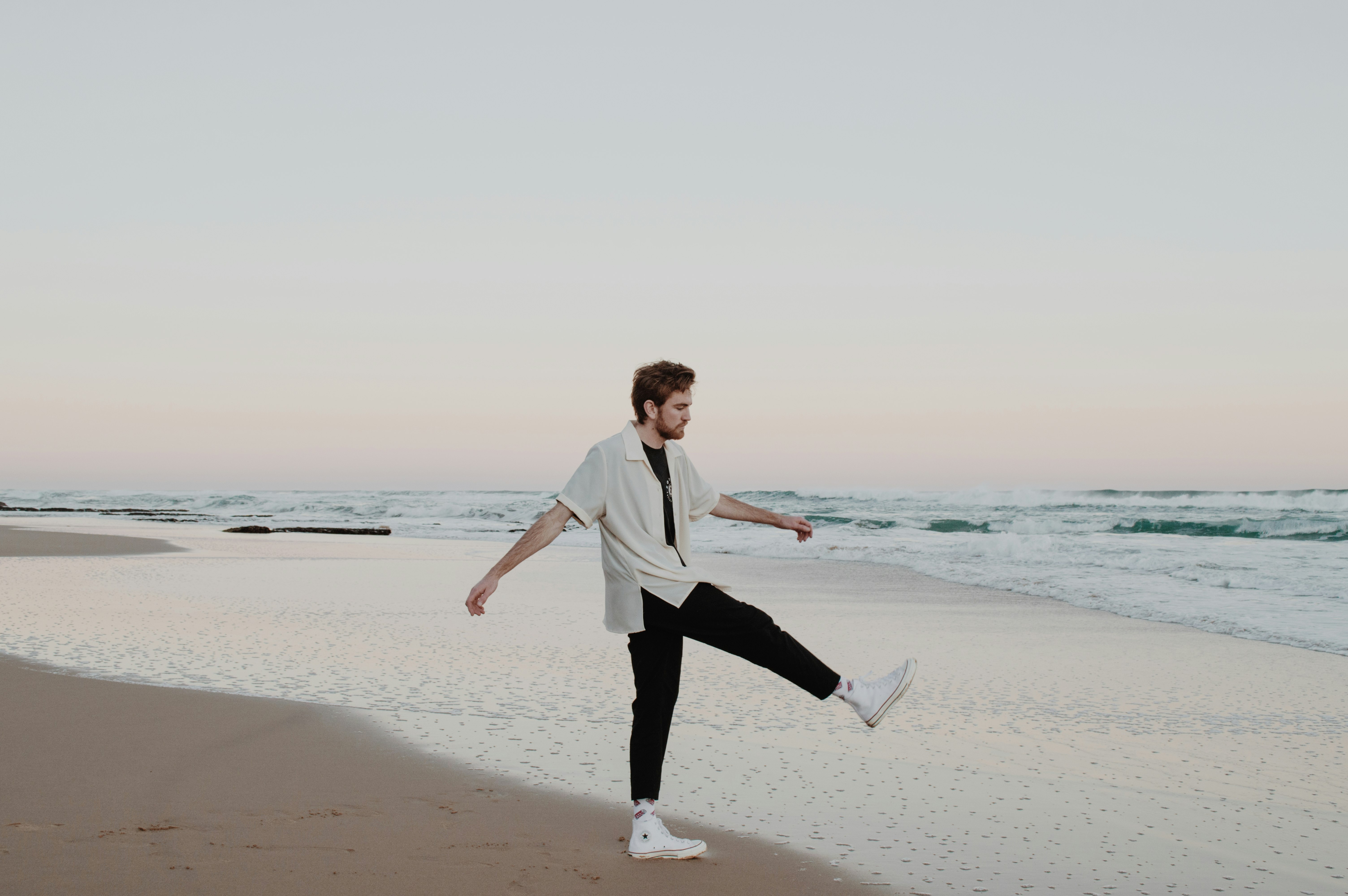 woman in white blazer and black pants walking on beach during daytime